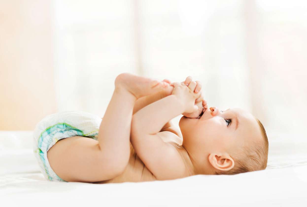 Un bébé en couche sur le dos qui joue avec ses pieds