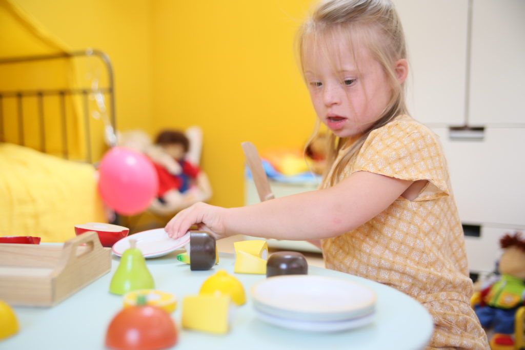 Une jeune fille avec trisomie 21 jouent avec des aliments en plastique