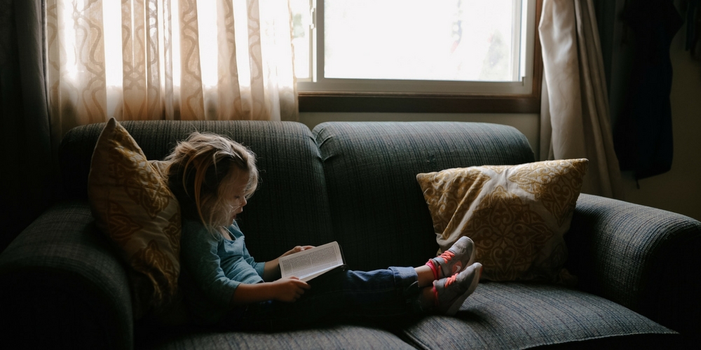 Une enfant lit sur le canapé