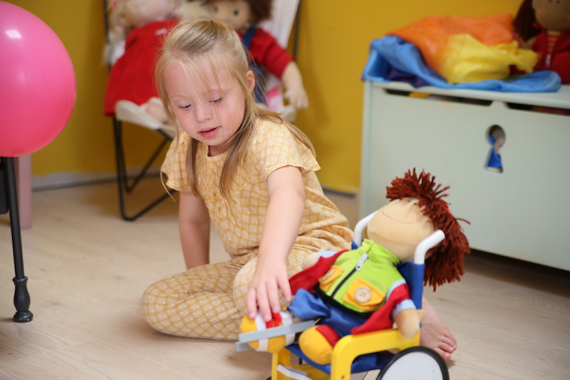 Niña con síndrome de down juega con un muñeco en silla de ruedas 