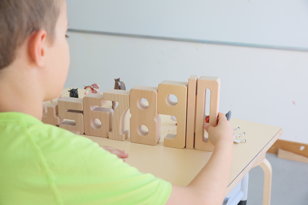 Un enfant joue avec des chiffres en bois allant du plus petit au plus grand