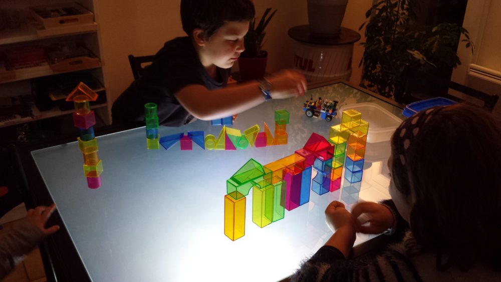 Des enfants jouent avec des blocs colorés sur une table lumineuse