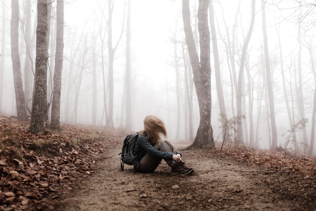 Jeune femme assise au sol dans la forêt. Elle est entourée de brouillard et ses cheveux sont dans son visage.