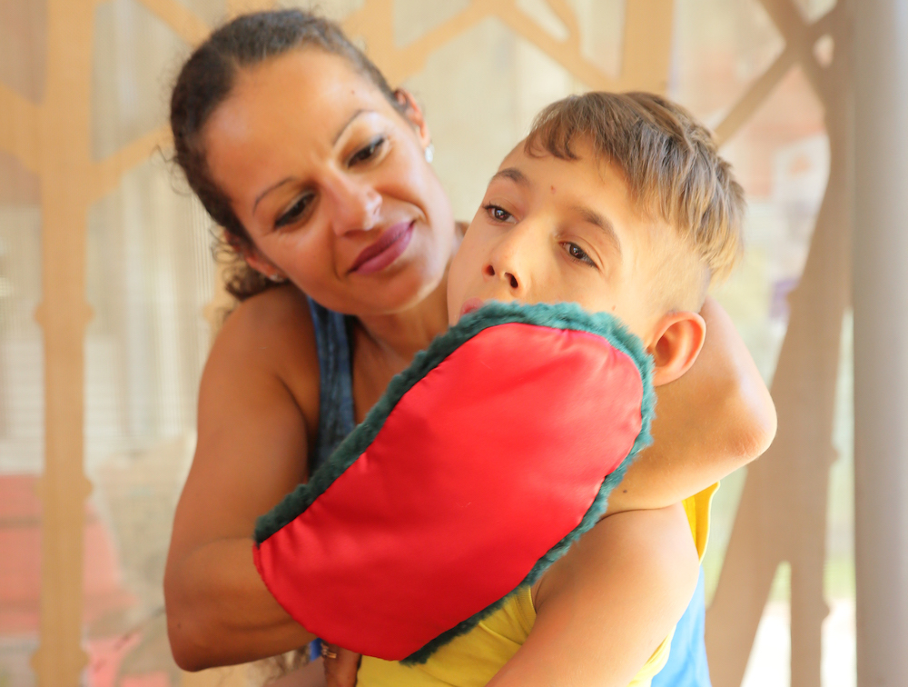 Niño con múltiples discapacidades al que se le acaricia la mejilla con un guante sensorial.