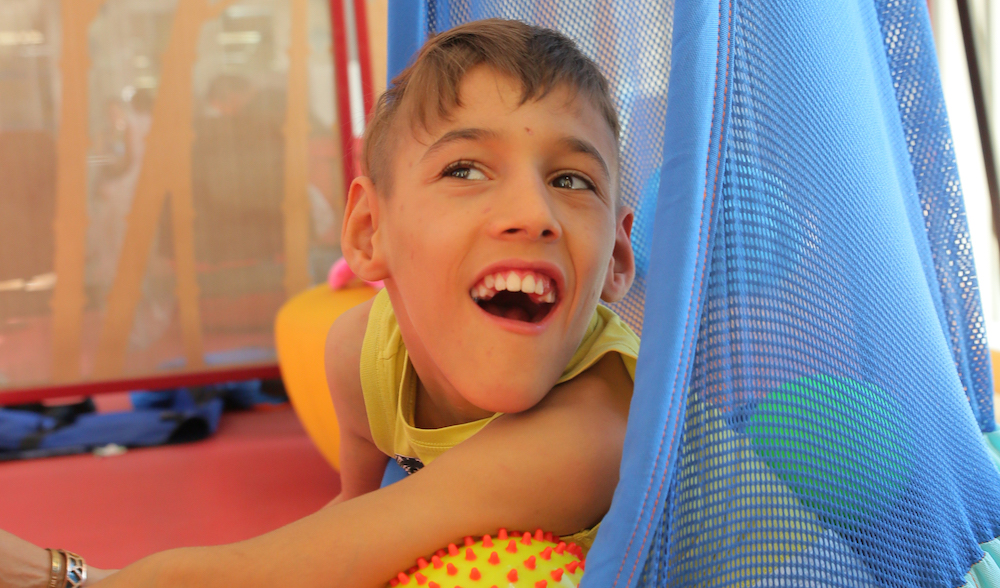 Enfant polyhandicapé qui est assis dans un nid hamac.