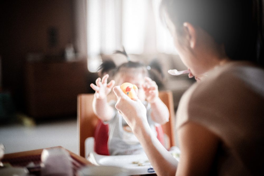 Une maman tient un jouet et une cuillère devant un enfant