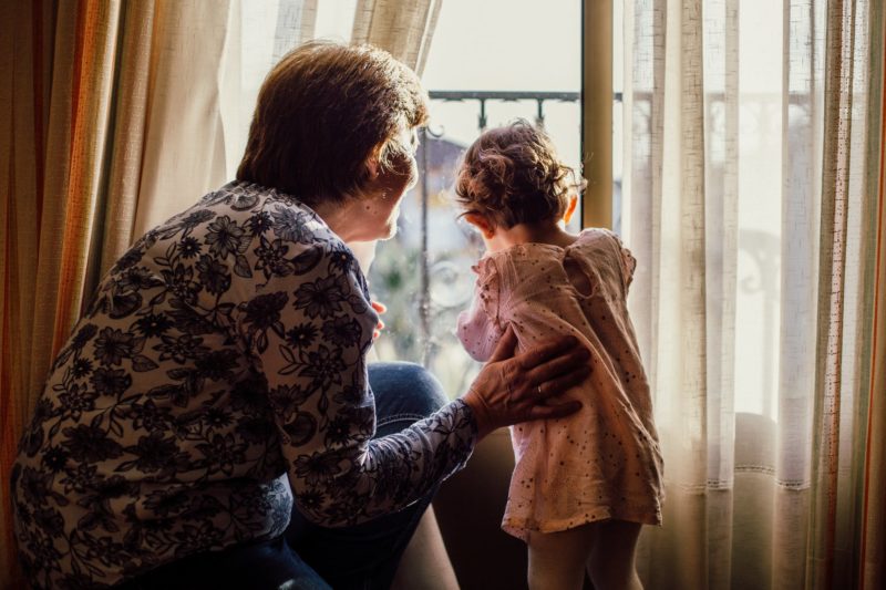 Une personne âgée avec une petite fille qui regardent par la fenêtre.