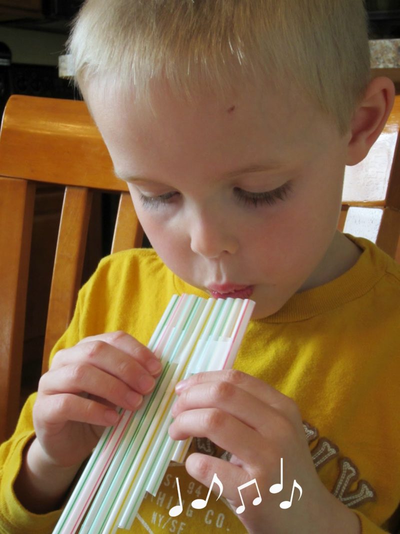 Un enfant joue d'une flûte de pan faites avec des pailles.