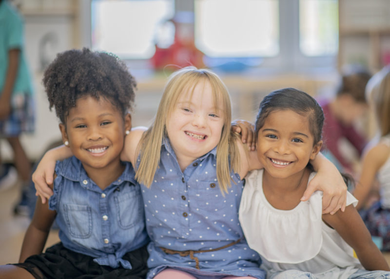 3 petites filles se tiennent par les épaules et sourient