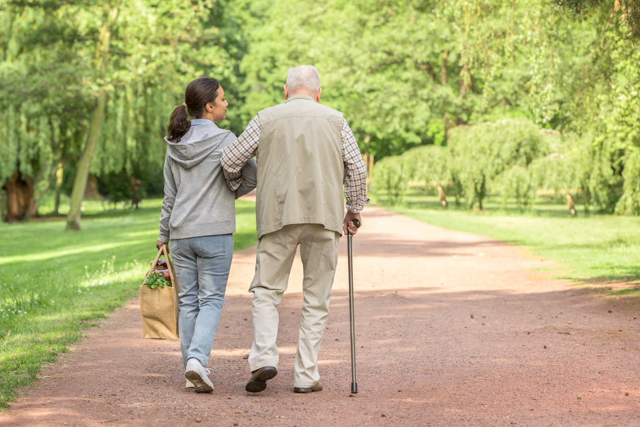 Une personne âgée qui marche en tenant le bras d'une femme plus jeune.