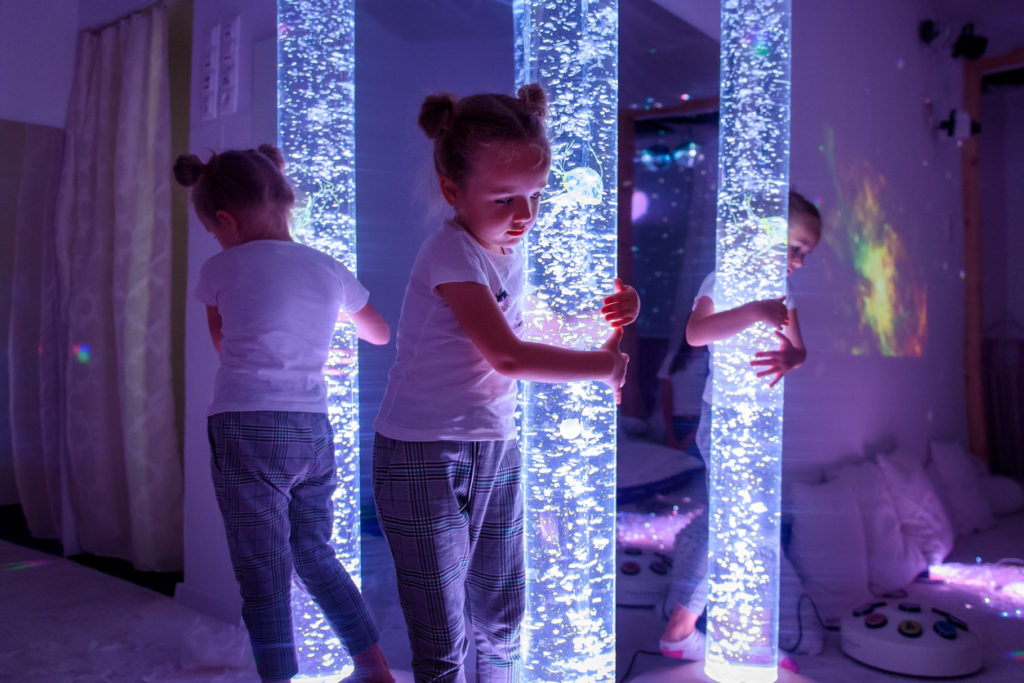 Une petite fille enlace une colonne à bulles dans une salle sensorielle