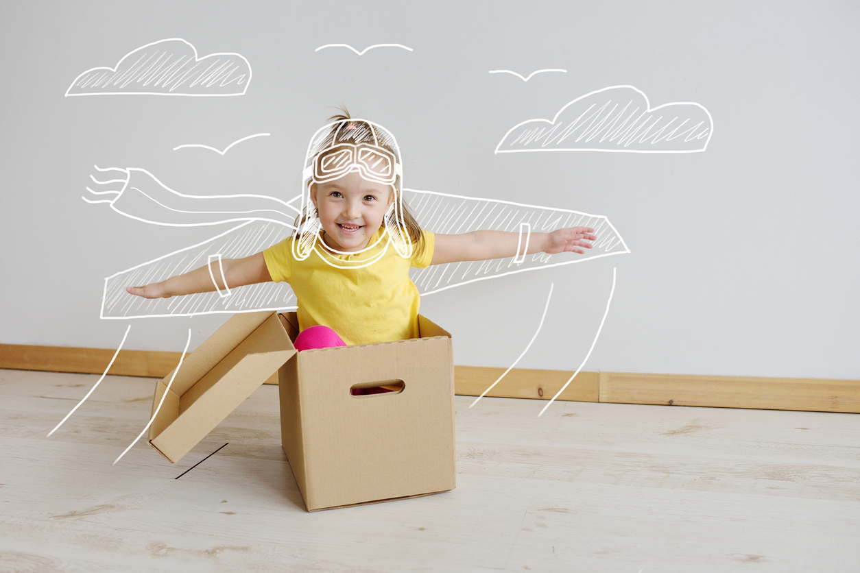 Un enfant dans un carton imite un avion en tendant ses bras