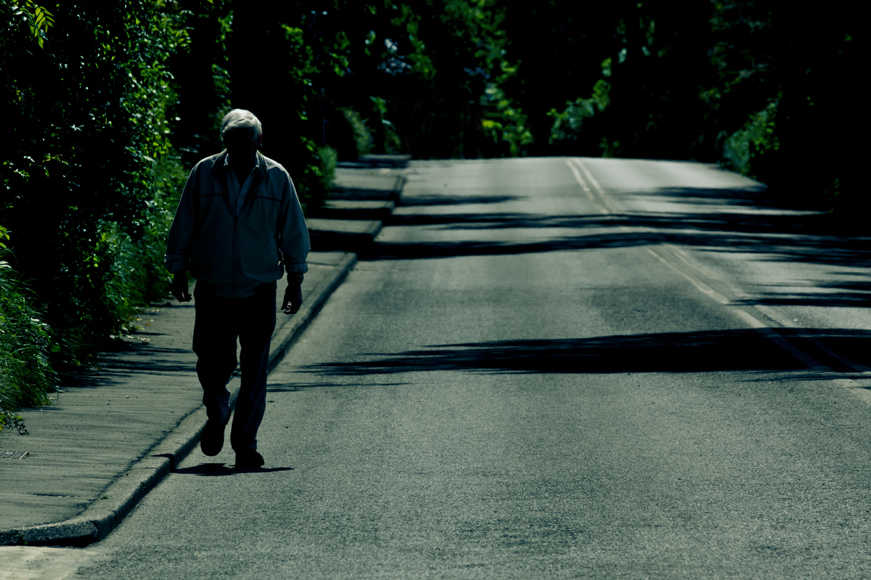 Un homme âgé marche sur une route déserte