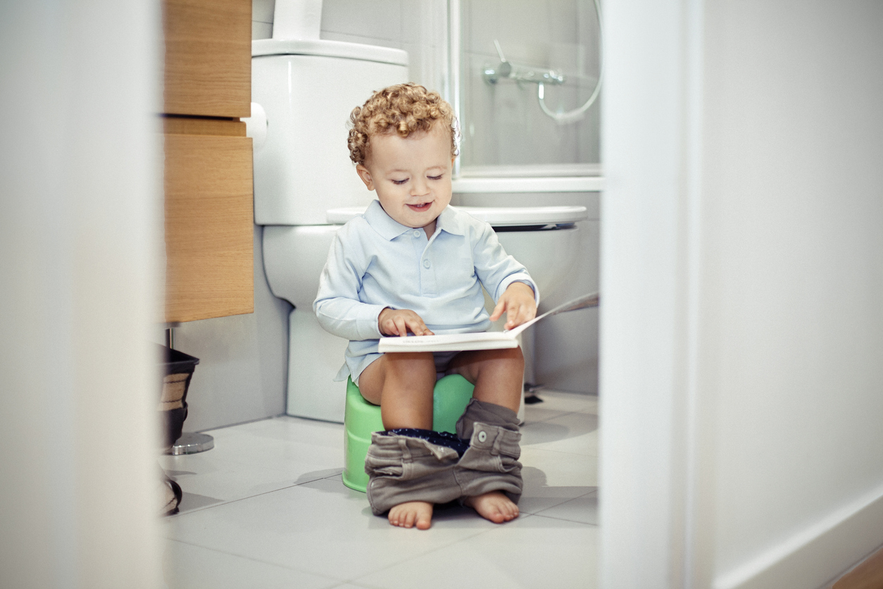 Enfant sur un pot d'apprentissage avec un livre dans les mains