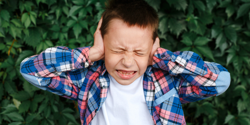 Un enfant se bouche les oreilles en grimaçant