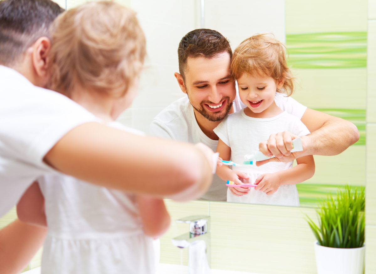 Enfant qui se brosse les dents avec son père devant le miroir.