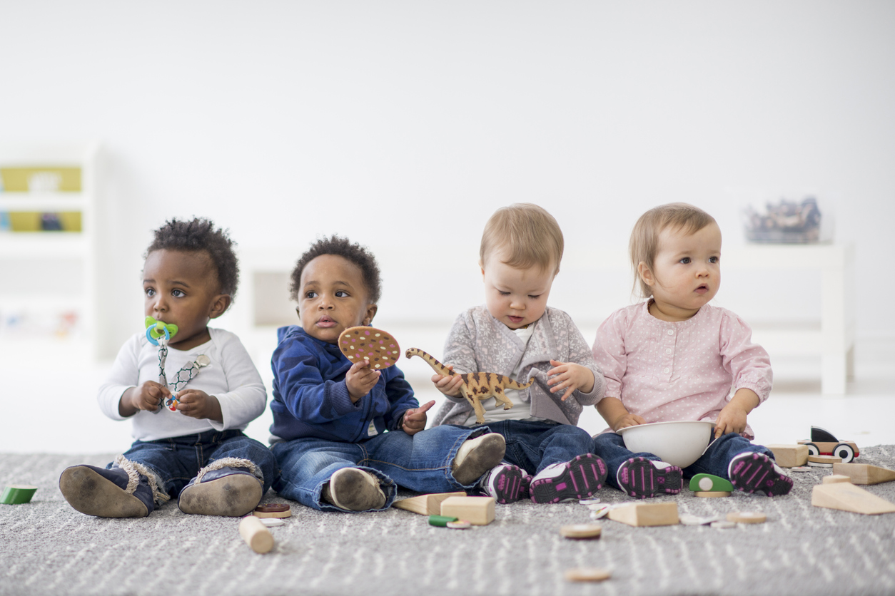 Un groupe de bébés jouent assis avec des jouets en bois et des figurines