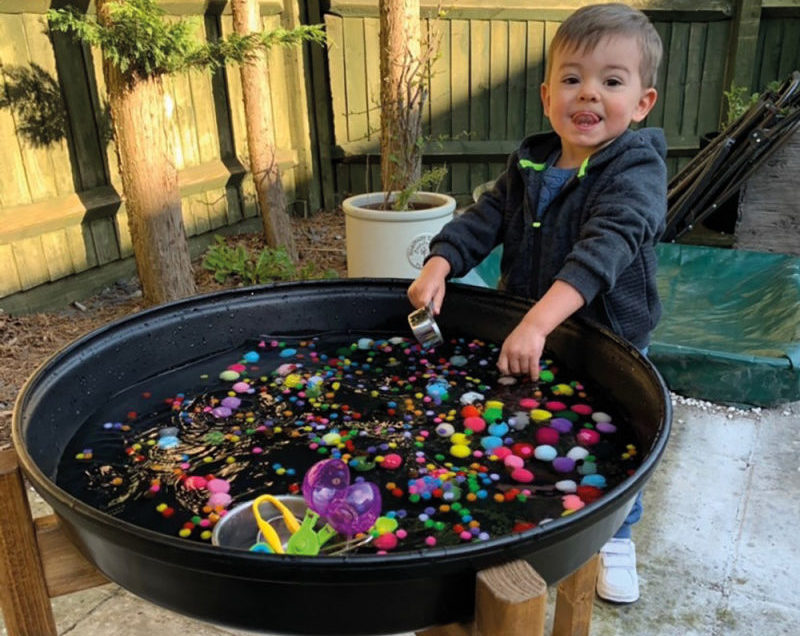 Un enfant fait une activité avec des pompons et de l'eau dans le bac d'exploration rond