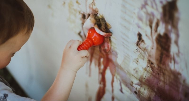 Un enfant réalise une peinture naturelle au mur.
