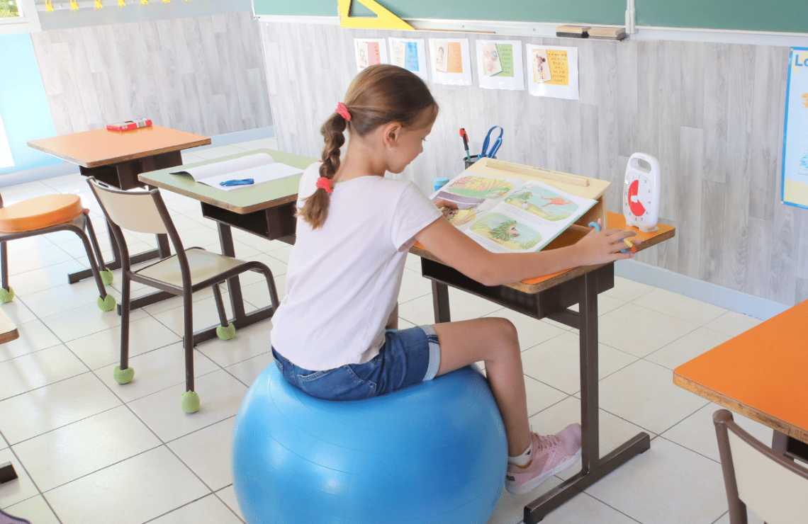 Une enfant assise sur un ballon d'assise dynamique dans une salle de classe