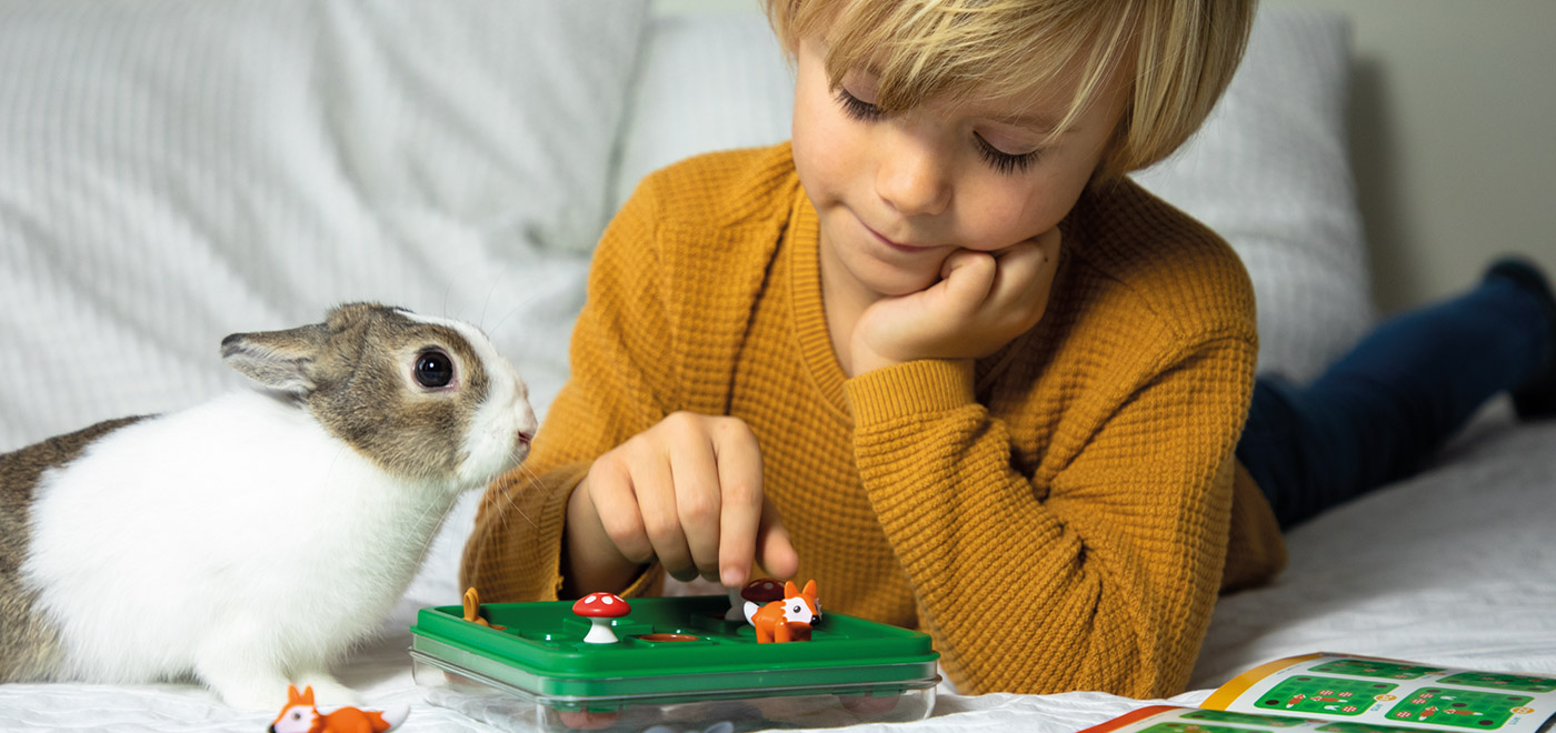 un nino tumbado jugando con un juego y un conejo