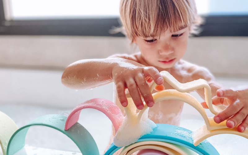 Un enfant joue avec des jouets en forme d'arc-en-ciel dans son bain