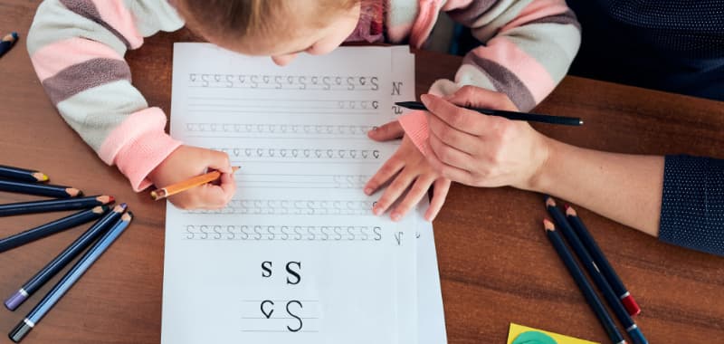 Un enfant écrit la lettre S sur une feuille