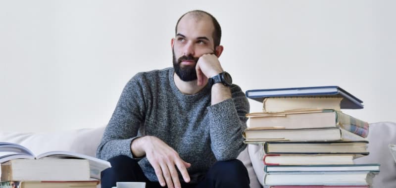 Un homme est dans ses pensées. Une pile de livres est posée devant lui.