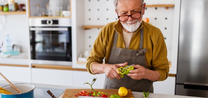 Un homme âgé coupe des poivrons dans une cuisine