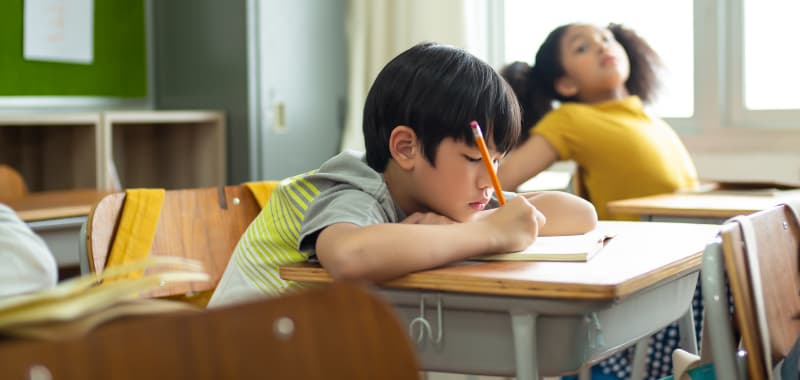 Un enfant écrit sur un cahier dans une salle de classe 