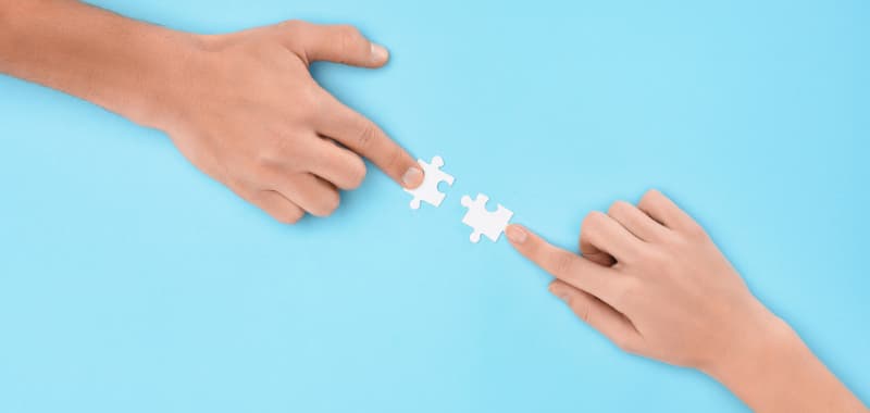 Image concept coopération : Deux mains rapprochant une pièce de puzzle sur fond bleu