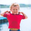 Un petit garçon blond montre les muscles de ses bras en riant