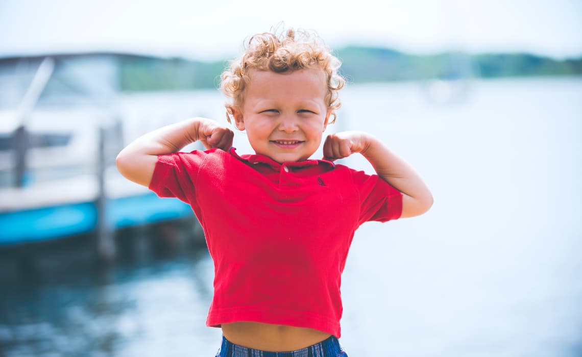 Un petit garçon montre ses muscles des bras en riant