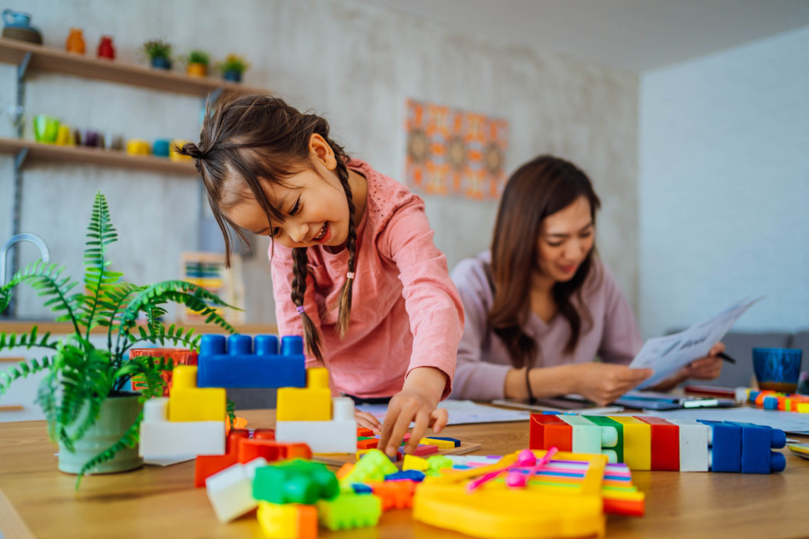 Une enfant jouent avec des Lego. Sa mère lit une notice en arrière-plan.