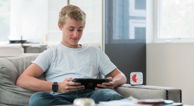 Un adolescent joue à la Switch. Un Time Timer est posé à côté de lui.