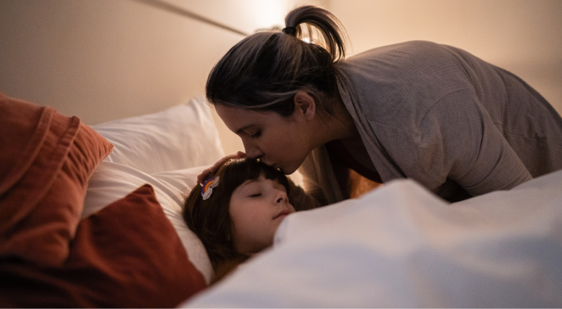 Une mère embrasse son enfant couché dans son lit sur le front.