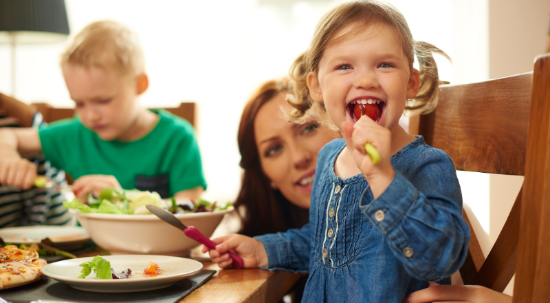 Une petite fille mange une tomate à table.