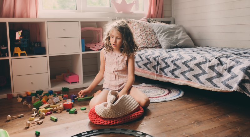 Une enfant est assise dans sa chambre. Ses jouets sont éparpillés autour d'elle.