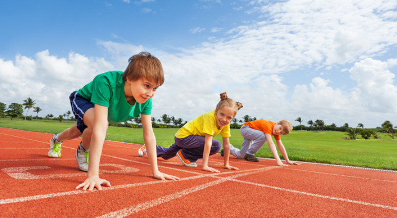 Trois enfants sur la ligne de départ d'une piste d'athlétisme