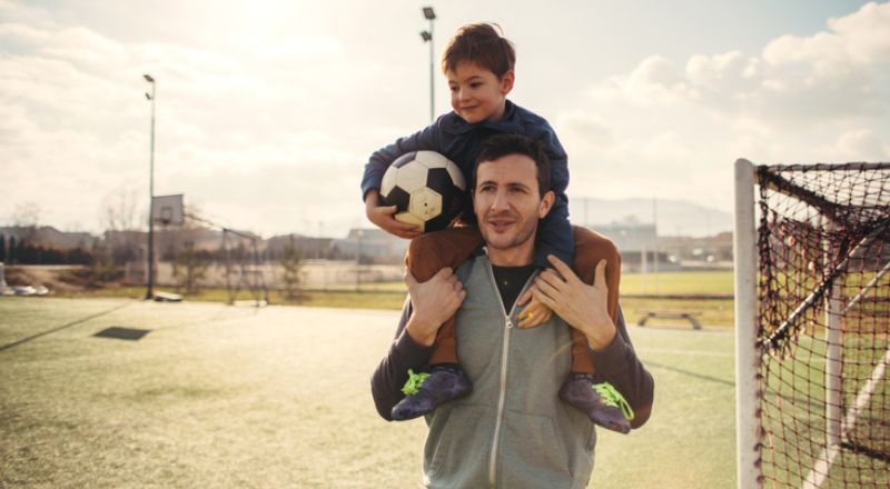 Un père et son fils sur ses épaules sont sur un terrain de foot