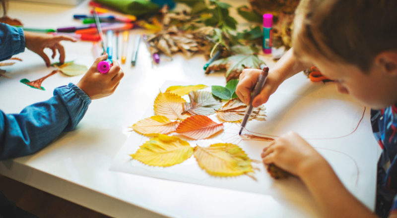 Un enfant fait une activité de dessin avec des feuilles d'arbre