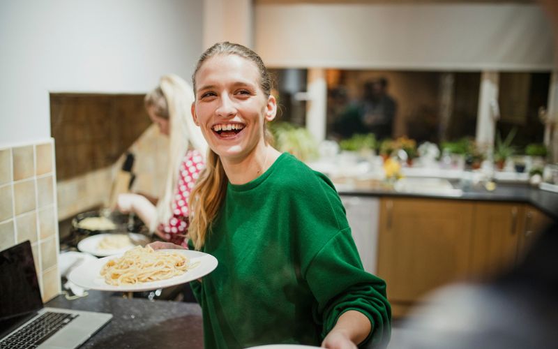Une jeune femme tient une assiette de spaghetti dans une cuisine