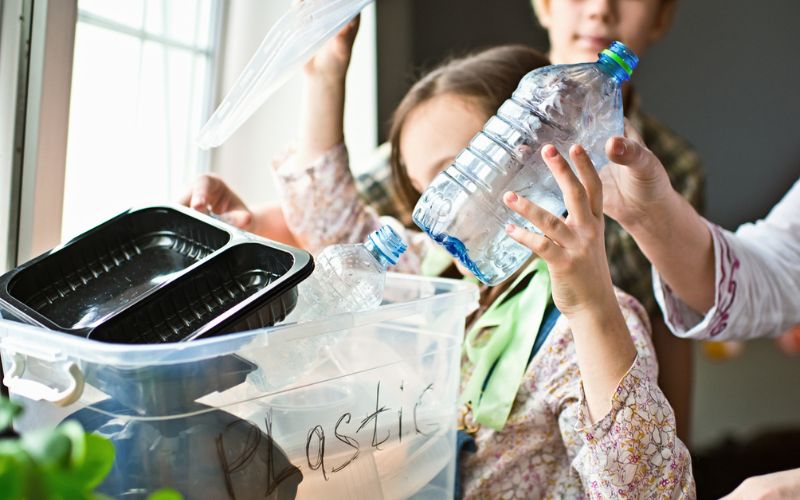 Une petite fille met une bouteille en plastique dans le bac de tri