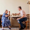 Un jeune homme est assis avec une personne âgée. Ils boivent du thé.