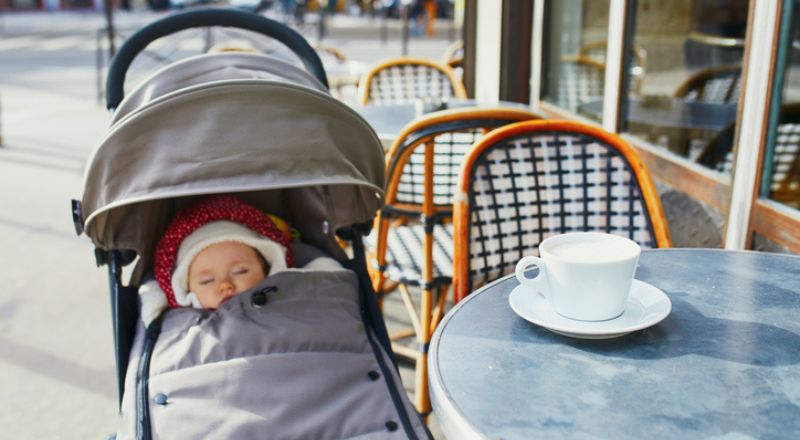 Un bébé qui dort dans une poussette à une table de café