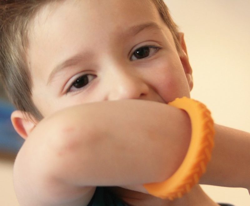 Un enfant mâche une bracelet Chewigem orange
