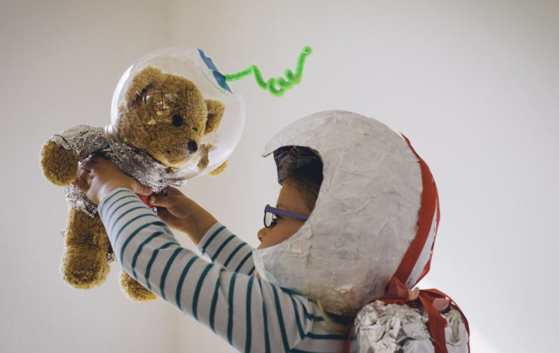 Un enfant déguisé en cosmonaute joue avec un ours en peluche