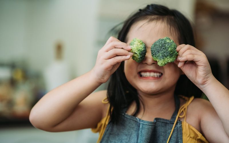 Une enfant tient deux brocolis devant ses yeux et grimace