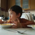 Un enfant attablé mange des spaghettis