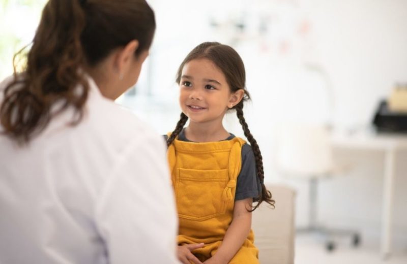 Une jeune fille en salopette jaune discute avec une médecin